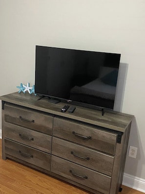 A television on a wooden dresser with drawers and a remote control. - Beach Days, Nightlife Nights, East End of PCB (Panama City)