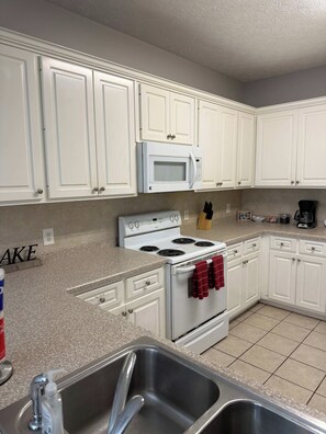 A kitchen with white cabinets, a white microwave, a stove, and a stainless steel sink. - Beach Days, Nightlife Nights, East End of PCB (Panama City)