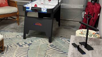 A room with a foosball table, a chair, a table with a remote control, and a wall-mounted item.