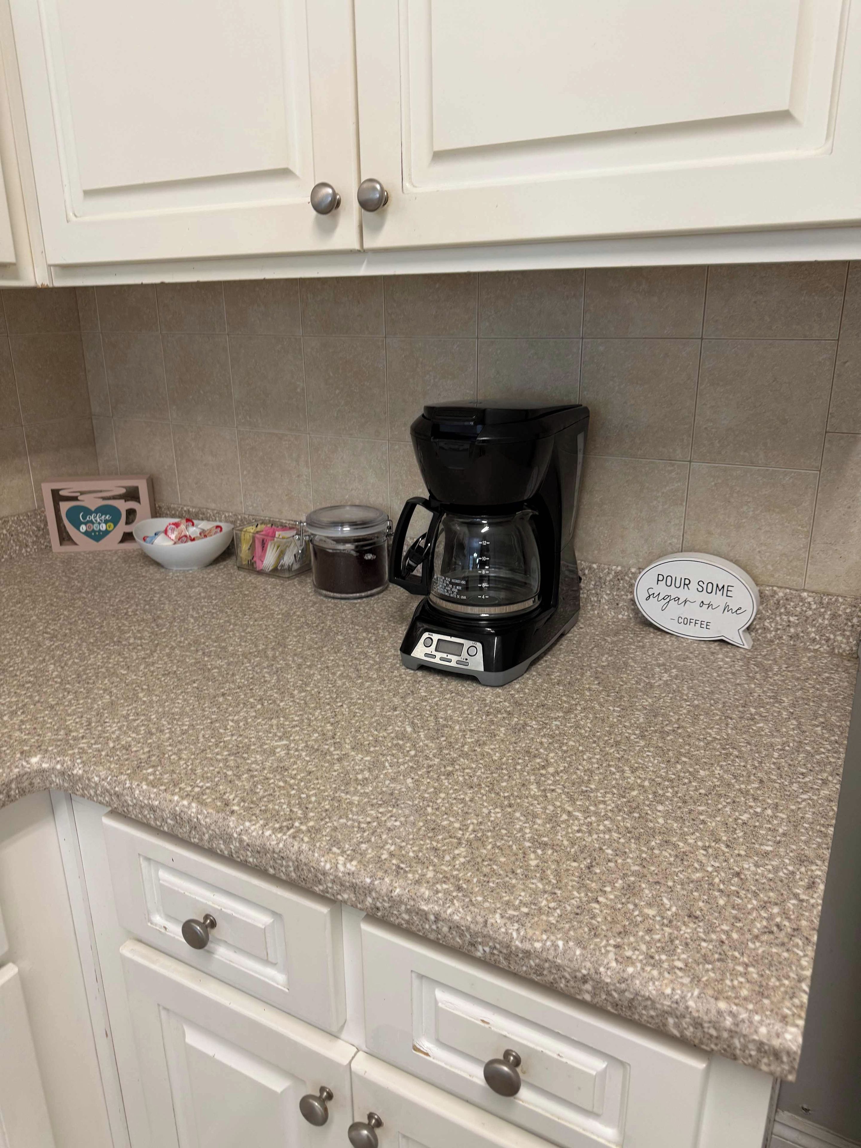 Een aanrecht met een koffiezetapparaat, een pot, een kom en een bord.