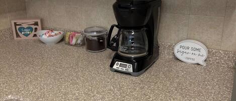 Uma bancada de cozinha com uma cafeteira, um pote, uma tigela e uma placa.