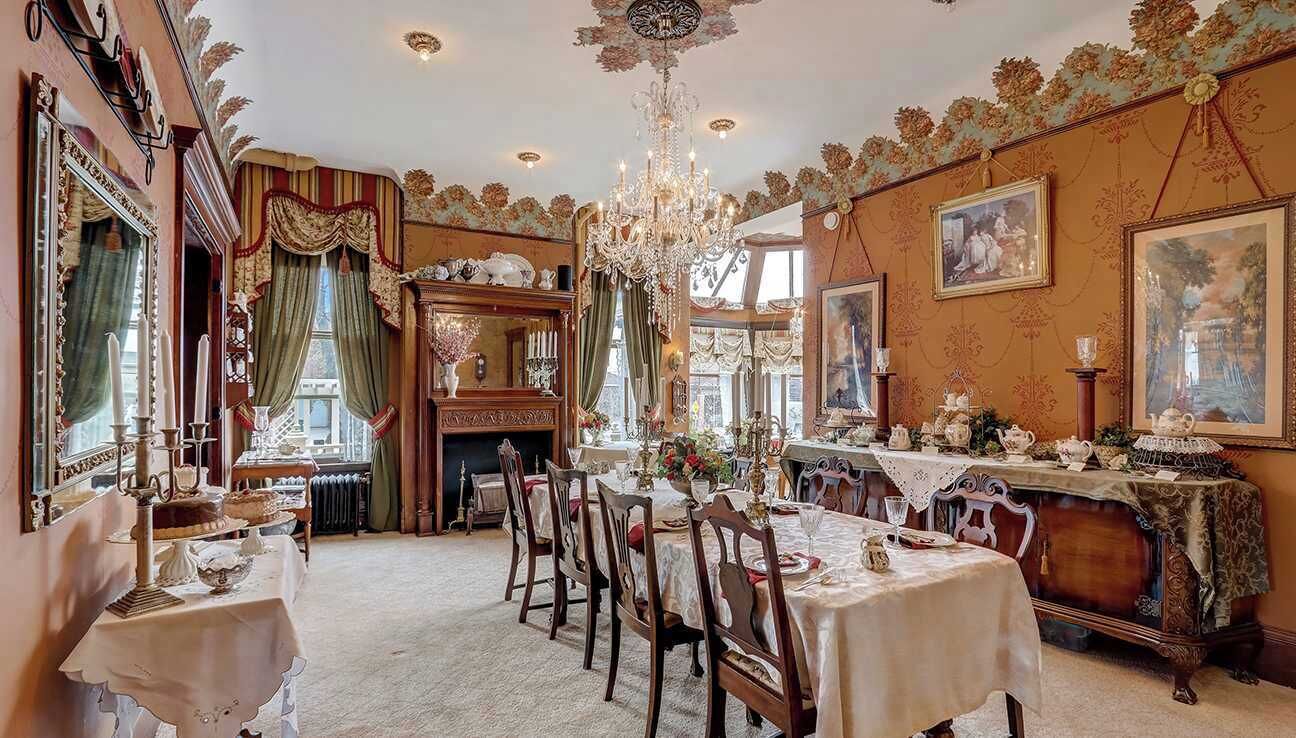 A formal dining room with a long table set for a meal, surrounded by ornate chairs and a chandelier.
