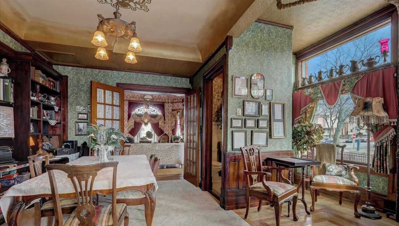 A dining area with wooden furniture, a chandelier, and a view of the street through a large window.