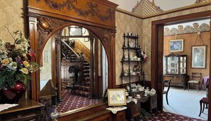 Um salão imponente com um espelho grande, uma escadaria e um armário de madeira com objetos decorativos.