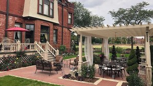 A patio area with outdoor seating, a pergola, and a brick building in the background. - Pias 2 Room Suite Queen Canopy bed 2nd floor (Milwaukee)