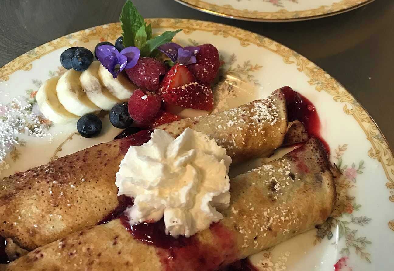 Ein Teller mit Crêpes, Blaubeeren, Erdbeeren, Bananenscheiben und Schlagsahne.