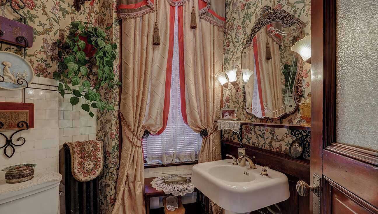 A vintage bathroom with floral wallpaper, a white sink, and a mirror with a decorative frame.