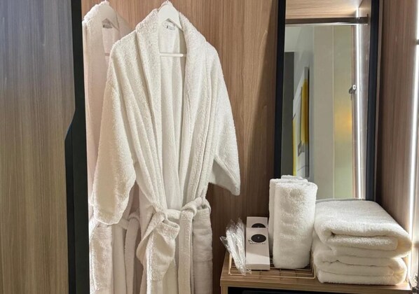 Une salle de bain d’hôtel avec un meuble-lavabo en bois, un peignoir blanc et des serviettes soigneusement pliées.