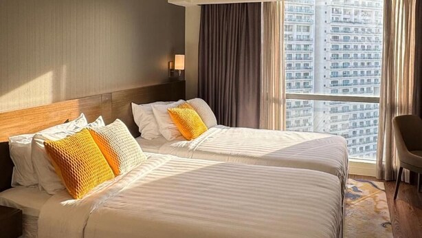 A hotel room with two beds, a view of a cityscape, and a large window with curtains. - Eleve Suites (Mandaluyong)