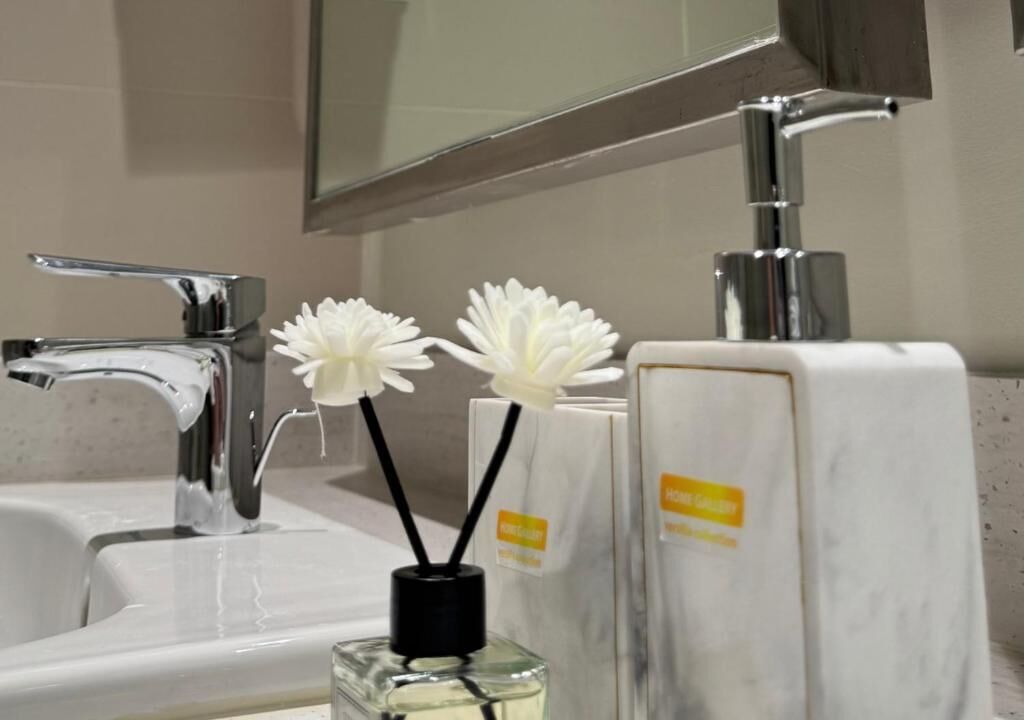 A bathroom sink with a chrome faucet, a mirror above it, and two white flower arrangements in a clear glass vase.