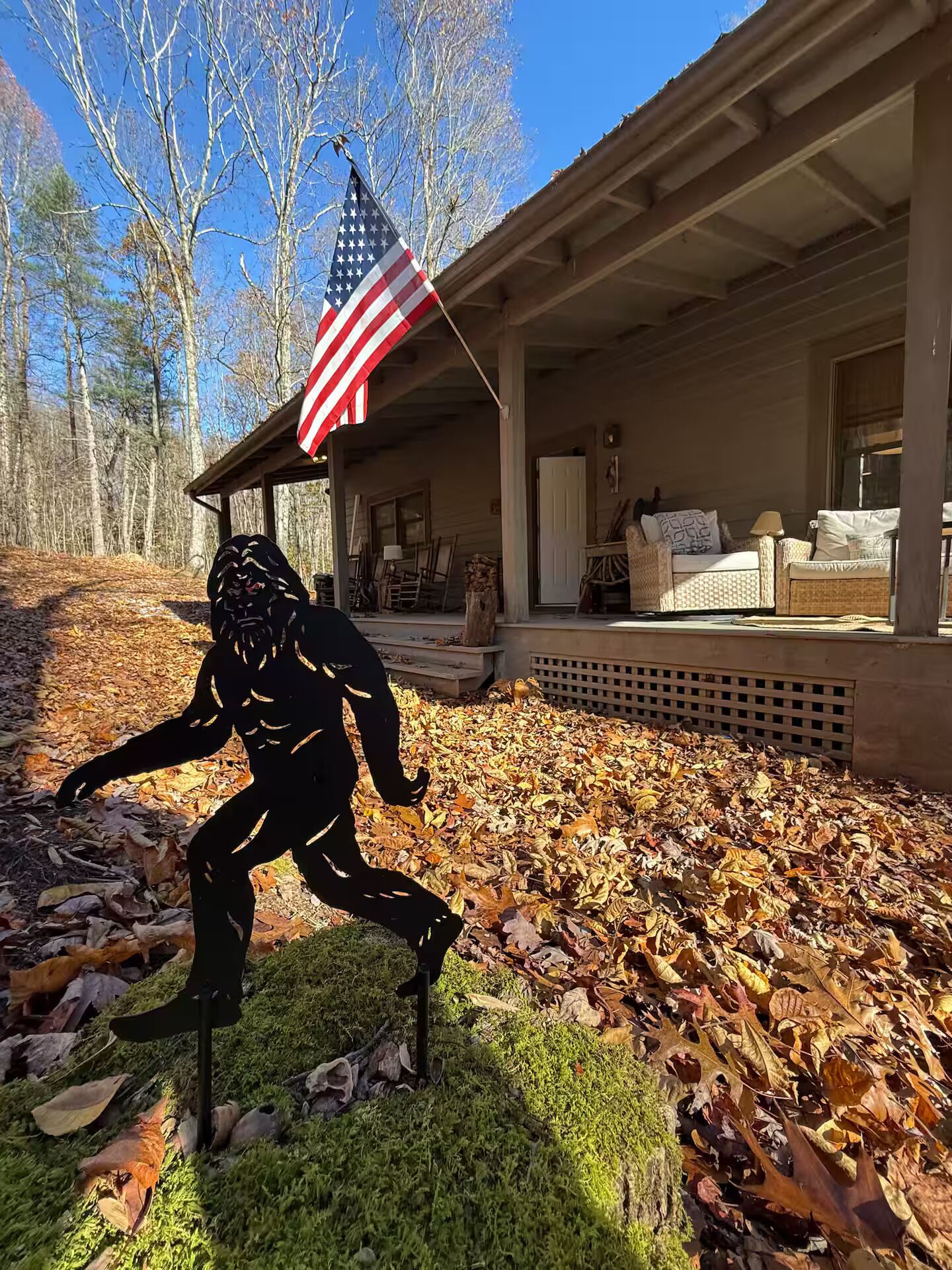 A rustic cabin with a porch, outdoor seating, and a large American flag.