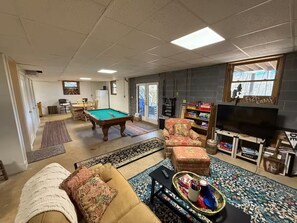 Un salon comprenant une table de billard, un canapé, un téléviseur et une bibliothèque.