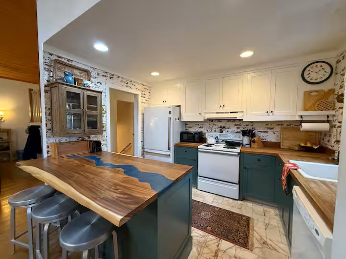 A modern kitchen with a central island, bar stools, white cabinets, a stove, and a microwave.