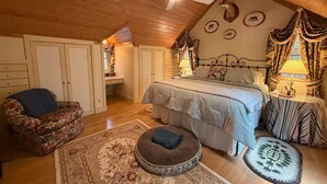 Un dormitorio acogedor en el ático, con techo inclinado, cama con ropa de cama floral, una silla y una alfombra.
