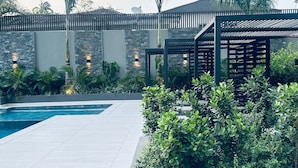 Ein moderner Außenpoolbereich mit Pool, Pergola und üppiger Bepflanzung.