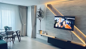 Ein modernes Wohnzimmer mit Flachbildfernseher an der Wand, einer Couch, einem Couchtisch und einem Essbereich mit Tisch und Stühlen.
