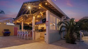 Un restaurante con terraza, techo de paja y luces colgantes.