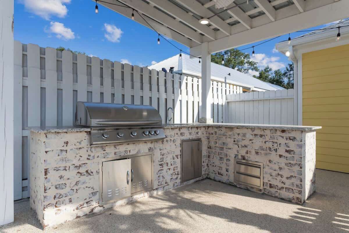An outdoor kitchen with a grill, storage cabinets, and a stone backsplash.