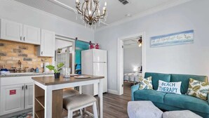 A modern kitchen with white cabinets, a wooden countertop, and a chandelier. There is a teal sofa with a pillow that reads "BEACH THERAPY" and a painting of swans on the wall. - Suite "Flamingo Pointe" with Shared POOL! (Bay St. Louis)