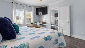 A bedroom with a bed, a ceiling fan, a TV, and a door leading to another room. - Suite "Flamingo Pointe" with Shared POOL! (Bay St. Louis)