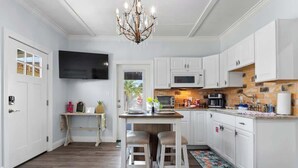 A modern kitchen with white cabinetry, a central island with stools, a chandelier, and a flat-screen TV mounted above the island. - Suite "Flamingo Pointe" with Shared POOL! (Bay St. Louis)