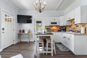 A modern kitchen with white cabinetry, a central island with stools, a chandelier, and a flat-screen TV mounted above the island. - Suite "Flamingo Pointe" with Shared POOL! (Bay St. Louis)