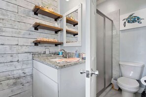 Une salle de bain avec un mur en bois rustique, un comptoir en granit, des toilettes blanches et un espace douche.
