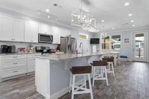 A modern kitchen with white cabinets, a large island with bar stools, stainless steel appliances, and a chandelier. - Family Home "Lone Star Cabana" Shared Pool! (Bay St. Louis)