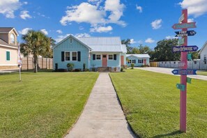 Uma casa com um jardim frontal e uma calçada que leva à entrada. Há um letreiro colorido com indicações para diversos locais.