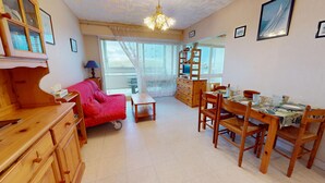 Ein gemütliches Wohnzimmer mit einem roten Sofa, Holzmöbeln, einem Esstisch für vier Personen und einem großen Fenster mit Aussicht.