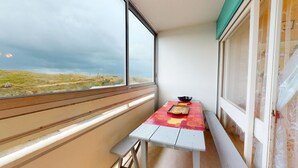 Ein Balkon mit Tisch und Bank, Blick auf eine grüne Landschaft und ein Fenster mit Vorhang.