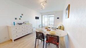 A bright dining area with a white table, black chairs, and a white cabinet. There are several small pictures on the wall and a window with a view. - Pause Atlantique - Sea view 100m from the beach (Saint-Gilles-Croix-de-Vie)