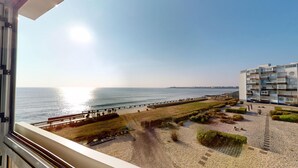 En vacker utsikt över kusten från en balkong med utsikt över en strand, en strandpromenad och en modern byggnad med balkonger.