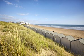 A beach with a row of beach huts, a sandy shore, and a grassy dune area. - Pause Atlantique - Sea view 100m from the beach (Saint-Gilles-Croix-de-Vie)