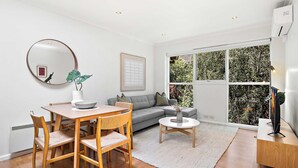 A modern living room with a dining table, sofa, and large windows. - South Yarra Apt | A/C, Parking & Easy Transport (South Yarra)