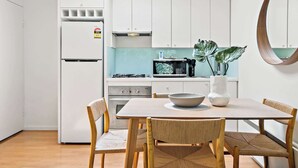 A modern kitchen with white cabinets, a microwave, a stove, and a dining table with chairs. - South Yarra Apt | A/C, Parking & Easy Transport (South Yarra)