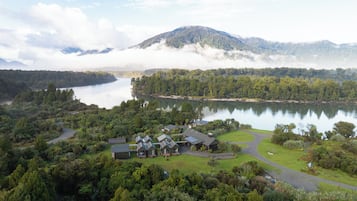 Un alojamiento con varias cabañas, un lago y una montaña boscosa al fondo.