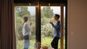 Une pièce dotée d’une grande porte-fenêtre coulissante donnant sur un jardin. À l’intérieur, on trouve une table en bois, sur laquelle sont posés un bol et une tasse.