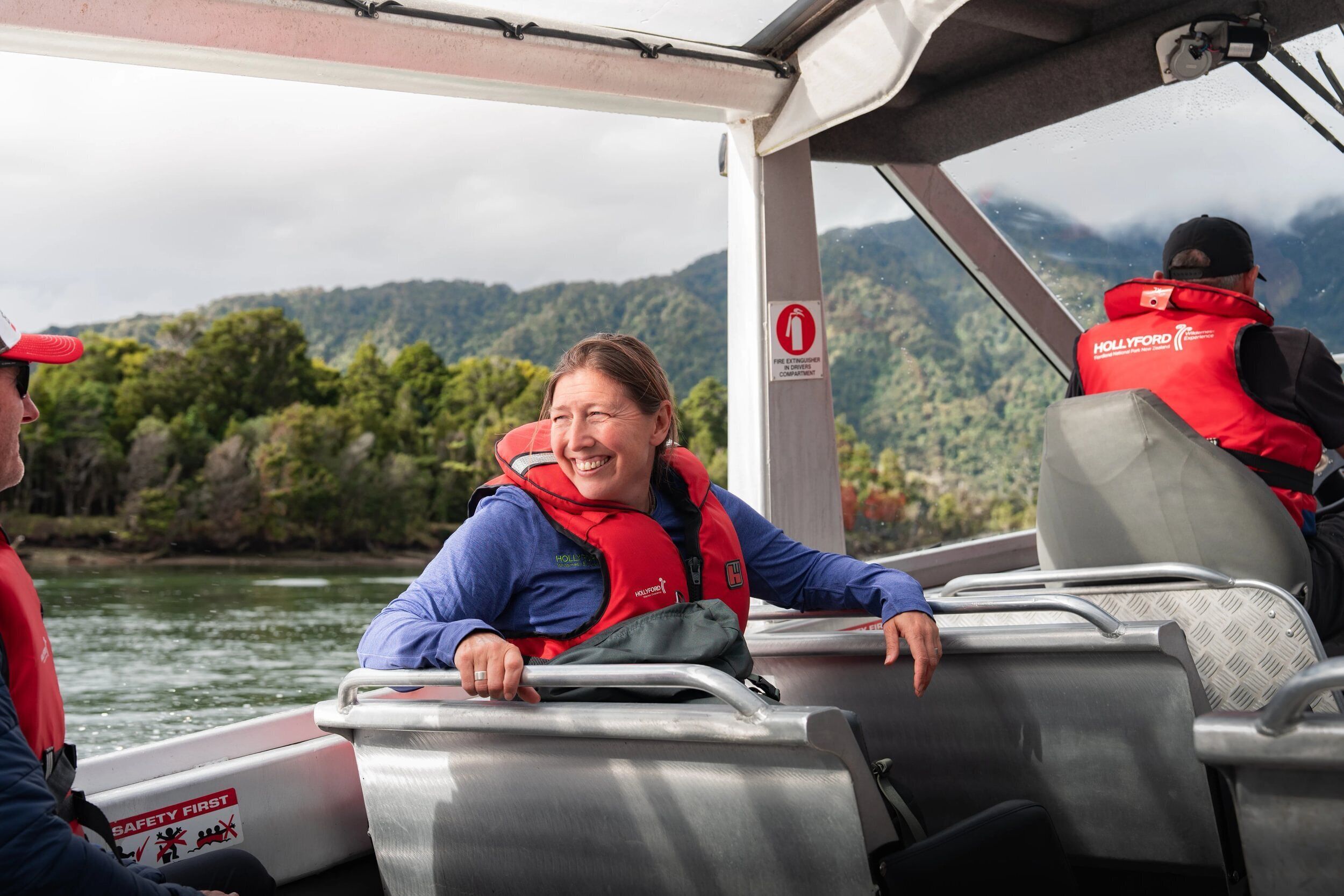 L’intérieur d’un bateau avec des passagers portant des gilets de sauvetage, un panneau indiquant « la sécurité avant tout », et une vue sur un paysage boisé.