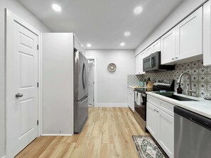 Eine moderne Küche mit weißen Schränken, einem Edelstahl-Kühlschrank, einer Mikrowelle und einer gemusterten Spritzschutzwand.
