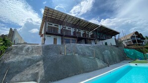 Un bâtiment moderne doté d’une piscine, d’un escalier menant à un balcon et surplombant un ciel d’un bleu éclatant.