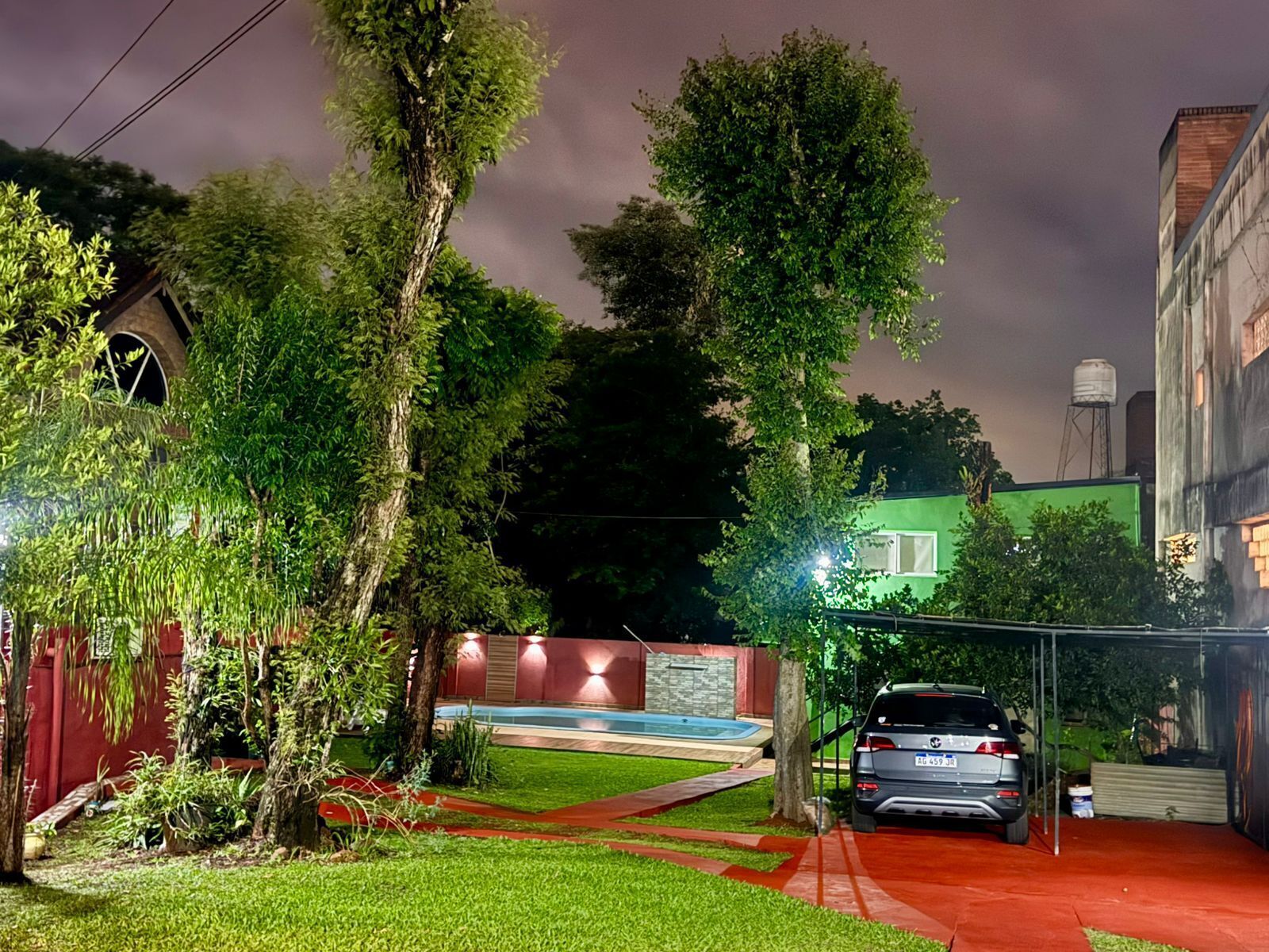 Un barrio residencial con un coche estacionado en la entrada, rodeado de árboles y un edificio de fachada verde.