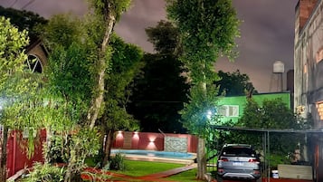 Un barrio residencial con un coche estacionado en la entrada, rodeado de árboles y un edificio de fachada verde.