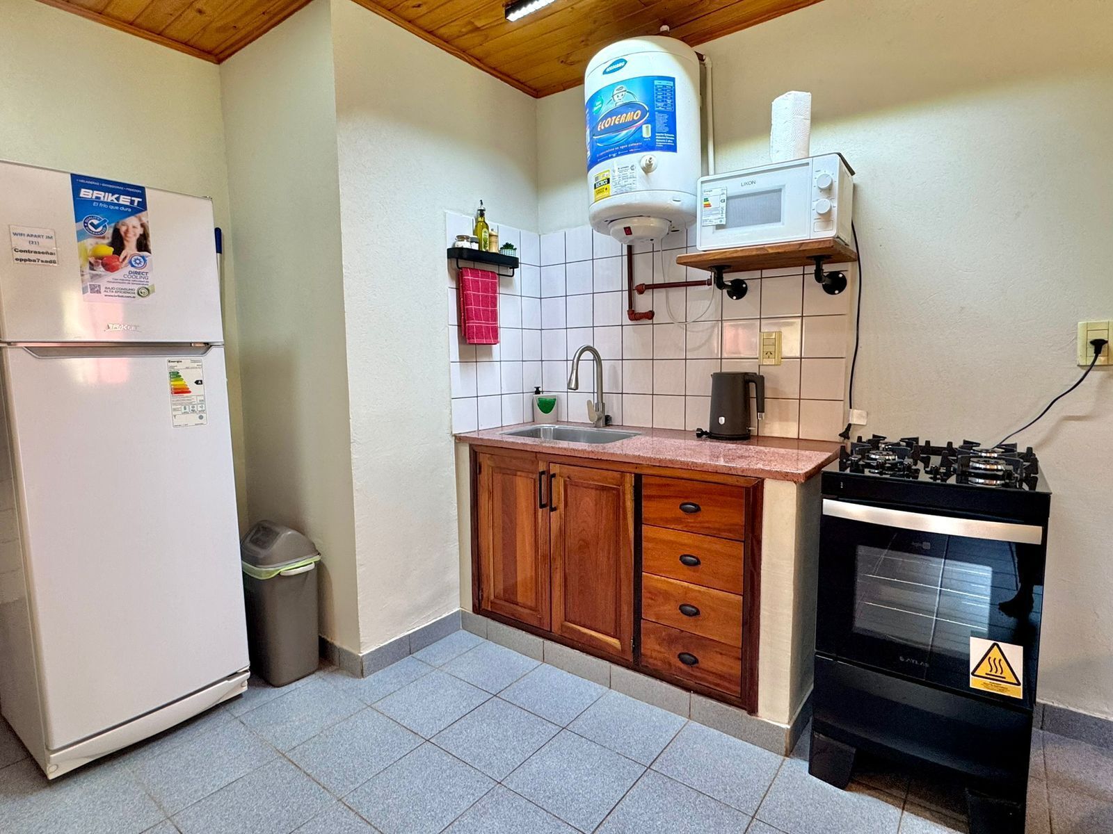 Cocina compacta con refrigerador, dispensador de agua, microondas, fregadero y estufa.