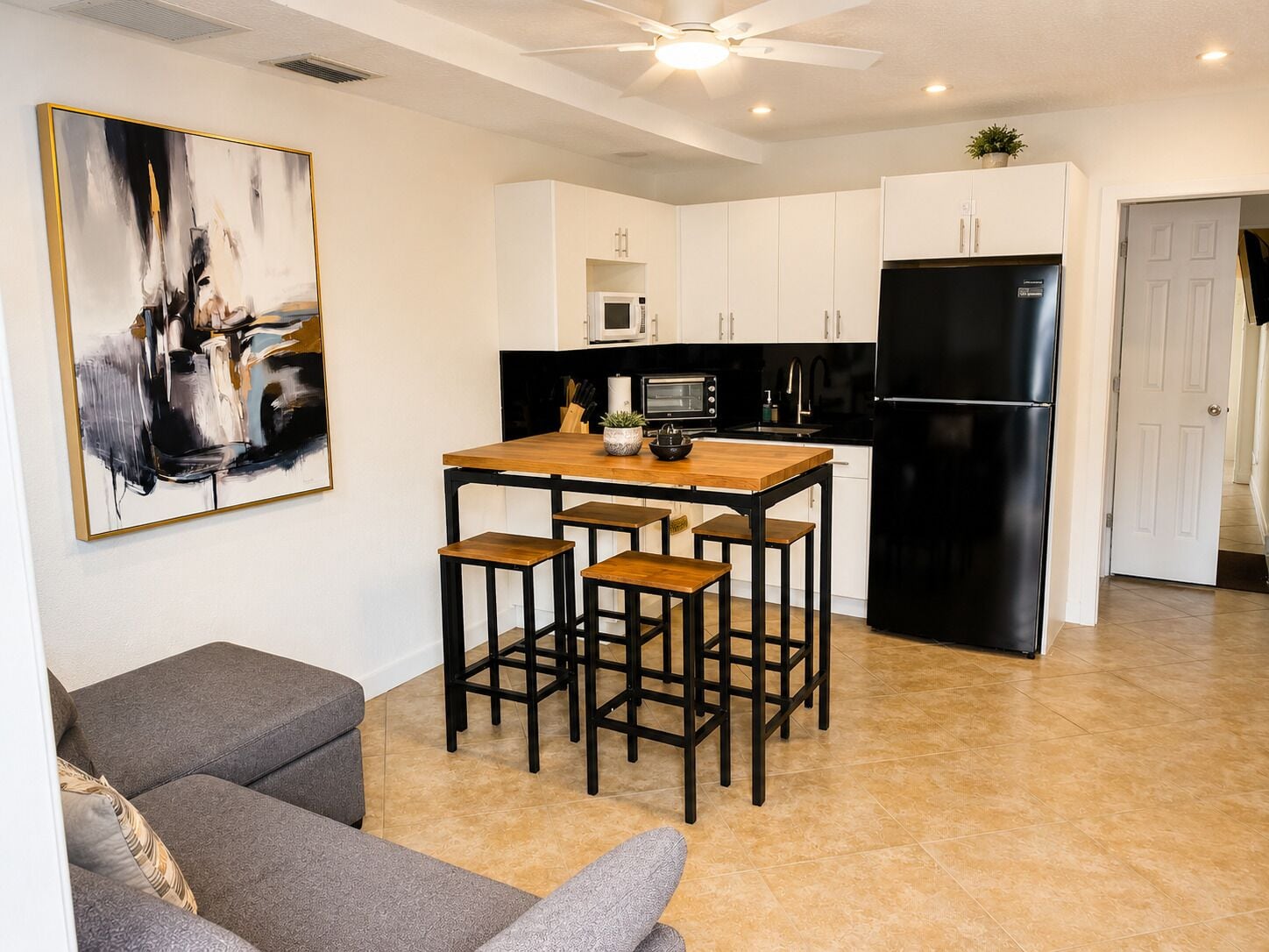Una cocina moderna con comedor, armarios blancos, refrigerador negro y ventilador de techo.