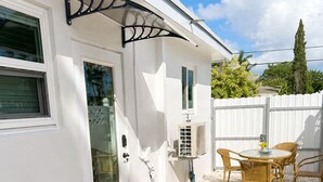 Een wit huis met een overdekte patio, een deur met een ruit en een klein terrasje met stoelen en een tafel.