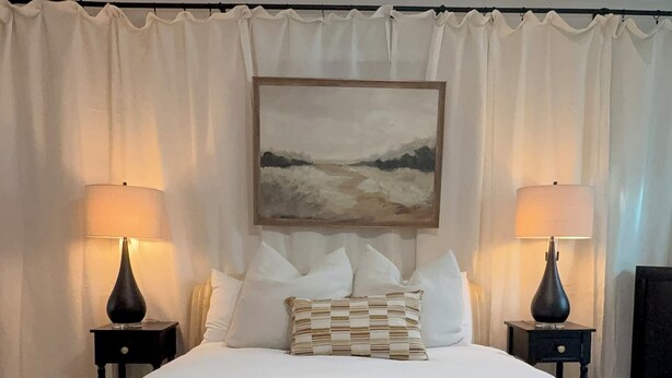 Een hotelkamer met een groot bed, twee bedlampjes, een plafondventilator en een schilderij aan de muur.