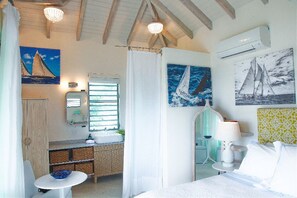 A room with a bed, a small table, a sink, and a mirror. There are paintings on the walls and a window with blinds. - SKY.   Beach Beach Beach Wake up to ocean views. Walk to the beach in 3 minutes! (St Pauls)