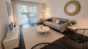 A modern living room with a sofa, coffee table, and chairs, a dining area with a table and chairs, and a large window with curtains.