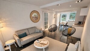 A modern living room with a sofa, coffee table, and chairs, a dining area with a table and chairs, and a kitchen area.